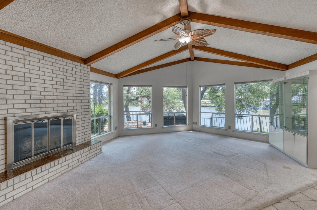 104 Bluebird Ln, Highland Haven, TX 78654 — living room with white brick fireplace, vaulted beamed ceiling and windows overlooking the lake, listed by D. Green & Associates